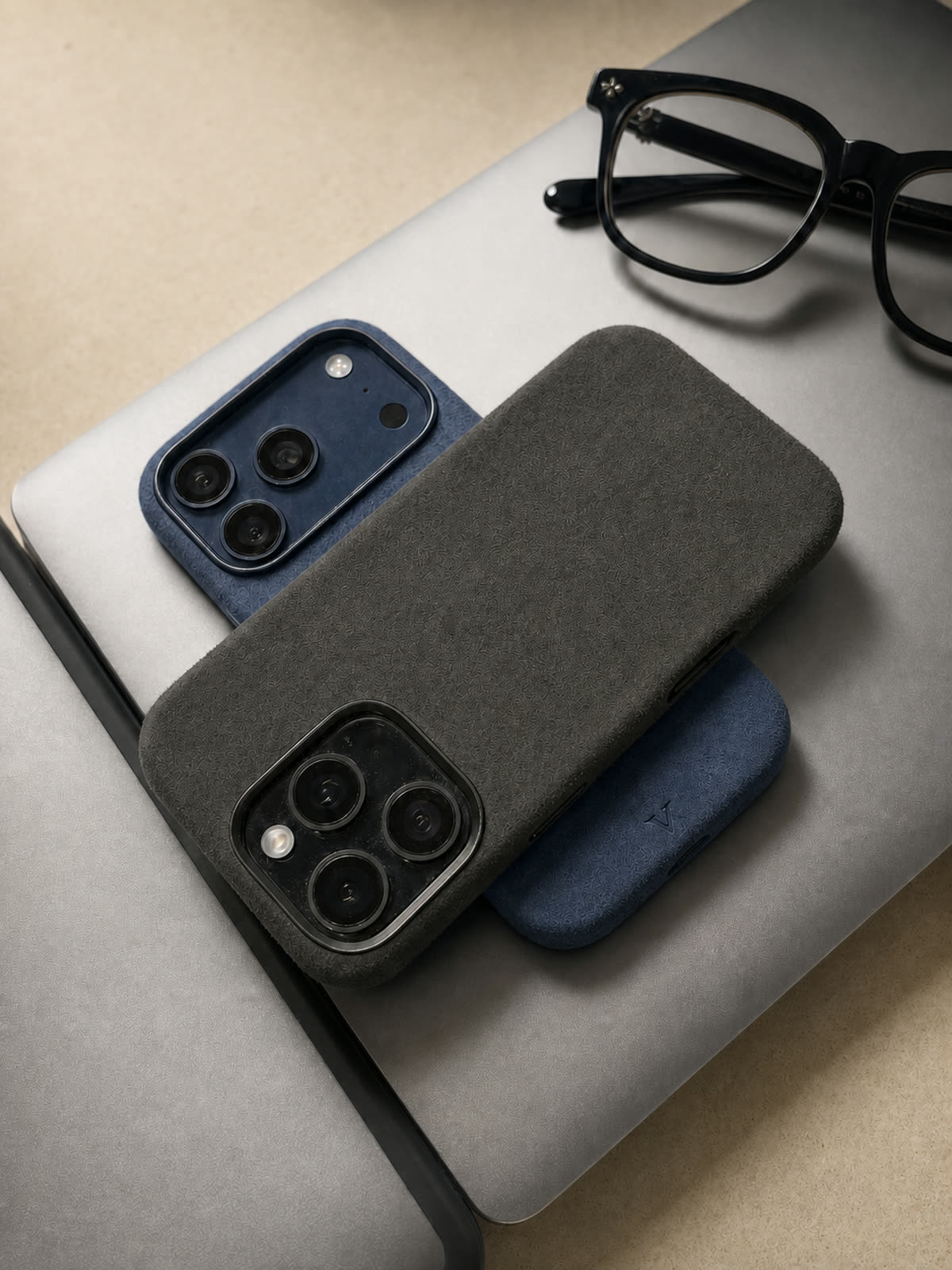Graphite and navy Virela iPhone 17 cases arranged on a laptop
